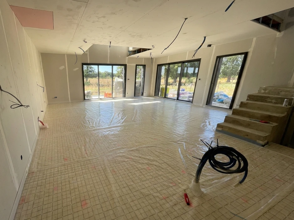 Chantier intérieur en cours, grande pièce de vie lumineuse avec dalle chauffante sous film polyéthylène de protection